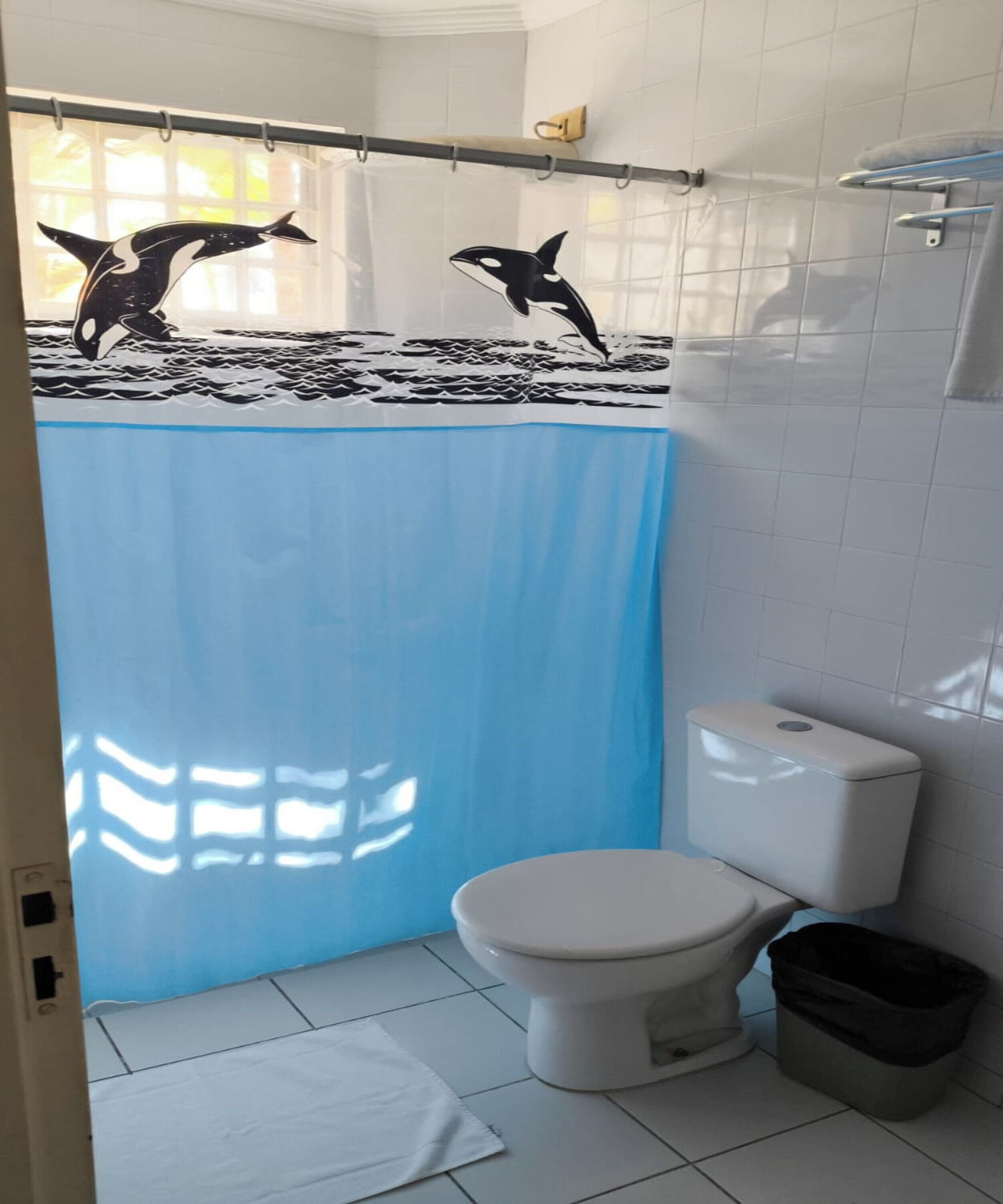 A bathroom with a white toilet, a blue shower curtain, and a black trash bin.