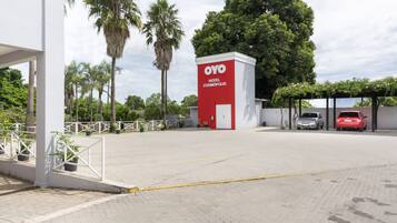 A hotel entrance with a red and white sign, palm trees, and a covered parking area.