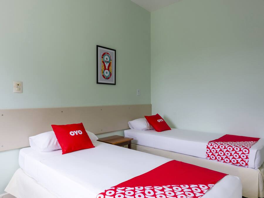 Two single beds with white bedding and red accents, a small wooden nightstand, and a framed abstract artwork on the wall.