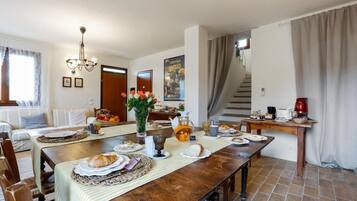 Un espace repas avec une table en bois dressée pour le repas, un lustre et un escalier menant à un autre niveau.