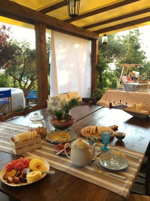 A dining table set outdoors with a variety of food items, a teapot, and a pitcher.