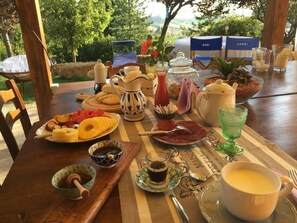 A breakfast table set outdoors with various food items, a coffee pot, and a pitcher of juice.
