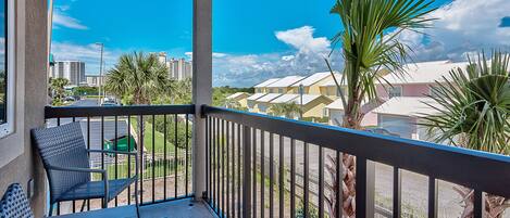A balcony with a view of a parking lot and buildings, featuring chairs and a railing.