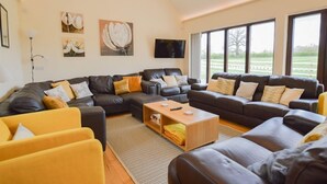 A spacious living room with a large L-shaped sofa set, a coffee table, and a flat-screen TV mounted on the wall. - The Cotswold Manor Court, Exclusive Hot Tub, Games Barn, 70 acres of Parkland (Bampton)