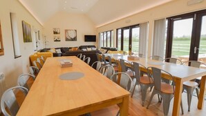 A spacious room with a long wooden table and chairs, a sofa set, and large windows offering a view of the outdoors. - The Cotswold Manor Court, Exclusive Hot Tub, Games Barn, 70 acres of Parkland (Bampton)