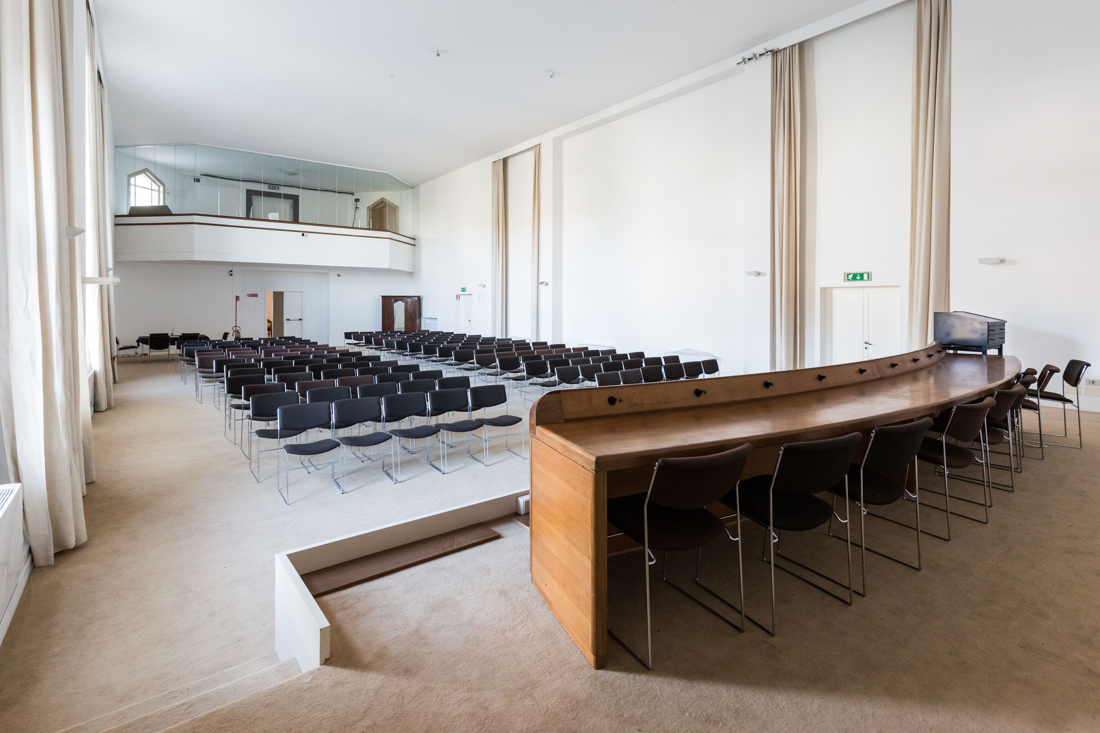 Une salle de conférence dotée d’une longue table et de chaises, de grandes fenêtres et d’un plafond haut.