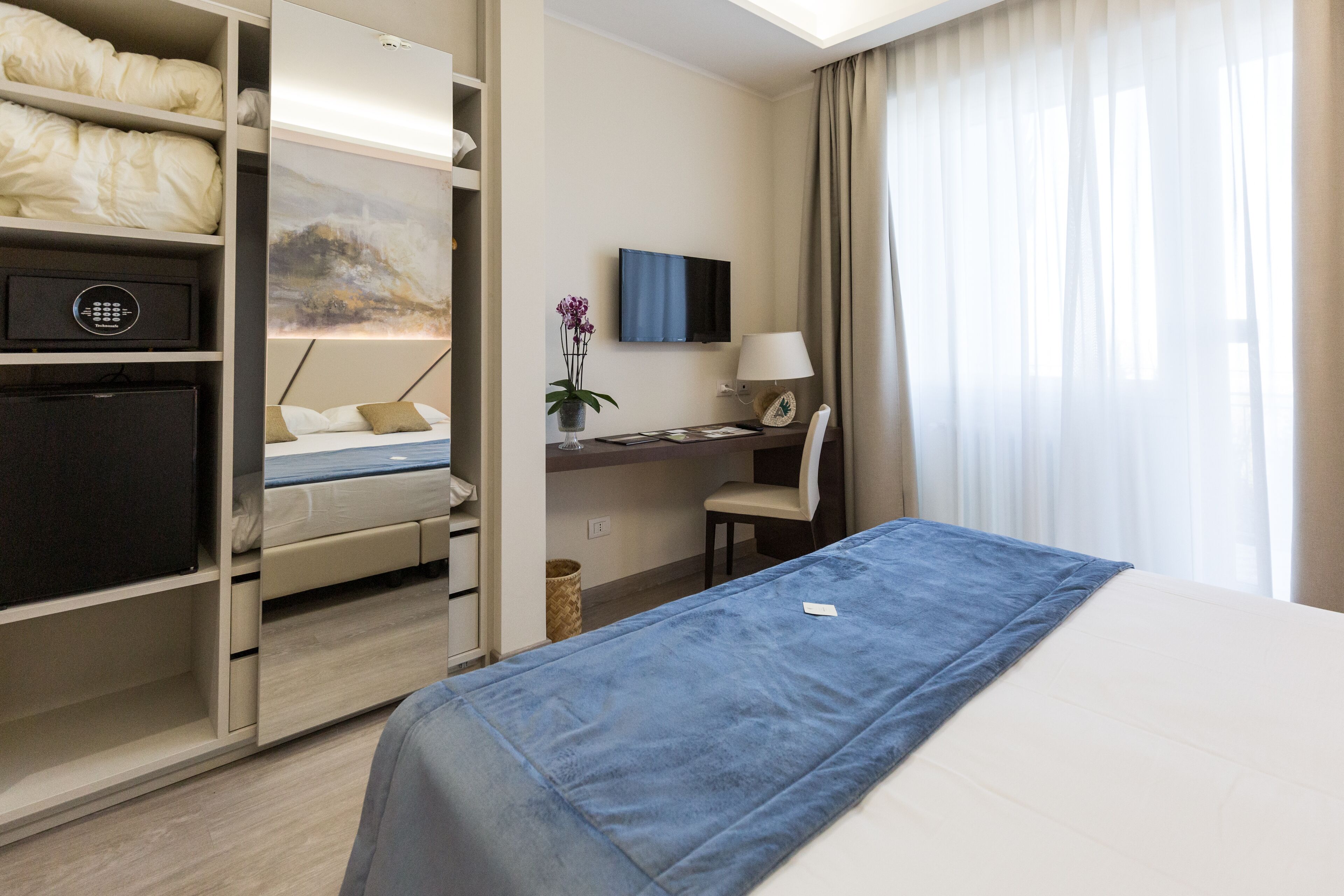 Een hotelkamer met een bed, een bureau met stoel, een televisie en een kledingkast.