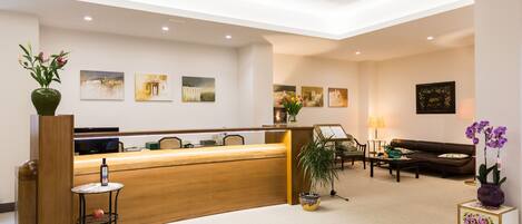 A hotel reception area with a wooden reception desk, a seating area with a sofa and chairs, and a reception counter.
