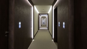 A long, narrow hotel corridor with doors on both sides, illuminated by overhead lighting. - Villa Cavalletti (Grottaferrata)