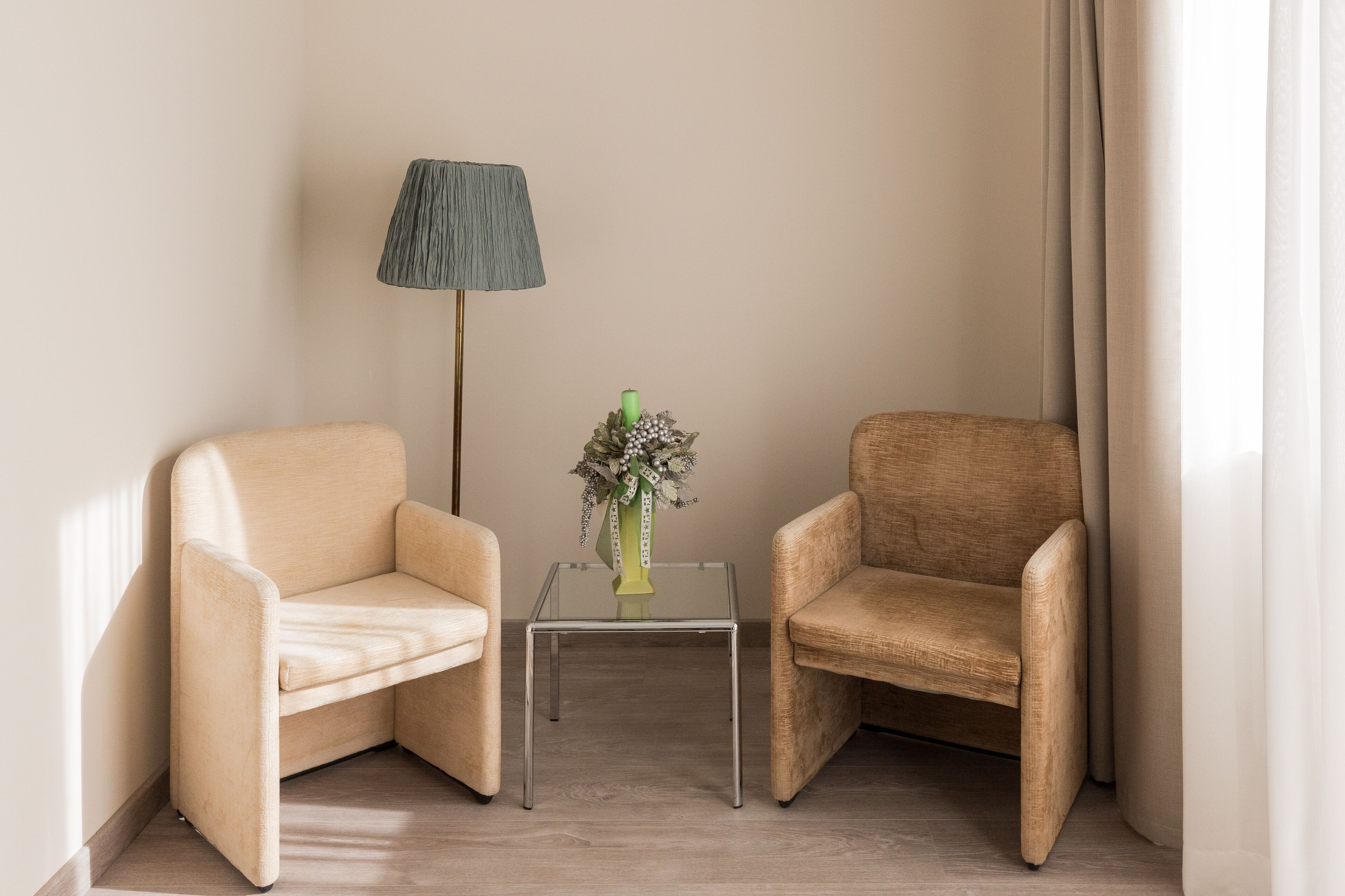 Una habitación con dos sillones color beige, una mesita de vidrio con un jarrón de flores y una lámpara de pie.