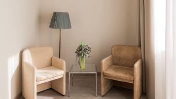 Una habitación con dos sillones color beige, una mesita de vidrio con un jarrón de flores y una lámpara de pie.