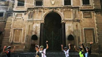 Un groupe de cyclistes se tient devant un bâtiment orné, doté d’une grande entrée en arc de cercle.