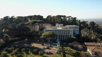Vista aérea de un hotel con un edificio central rodeado de árboles y coches aparcados.