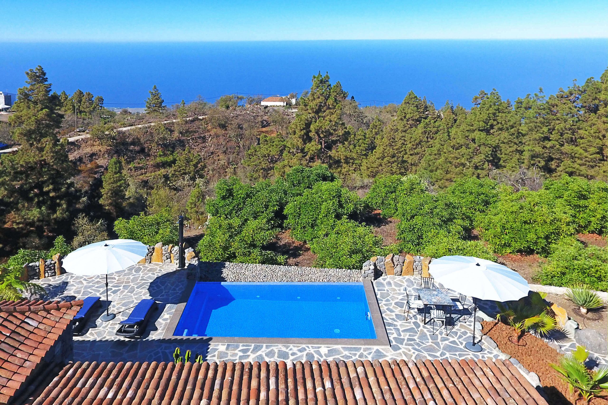 Une piscine sur le toit, agrémentée de deux parasols, entourée de carreaux de pierre et offrant une vue sur l’océan.