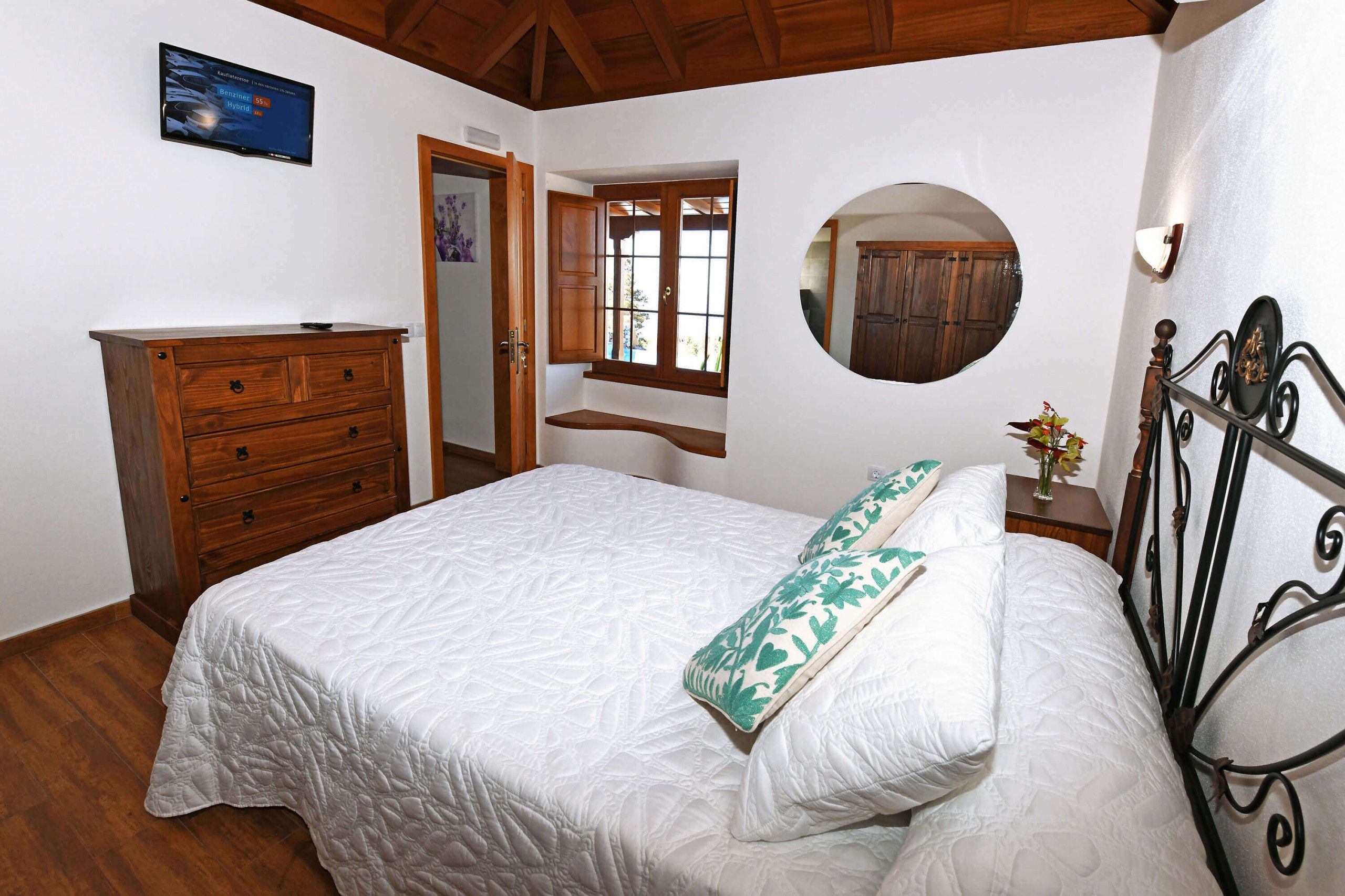 A bedroom with a bed, wooden dresser, a mirror, and a window.
