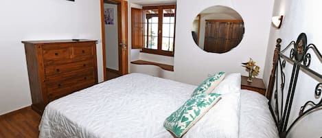 A bedroom with a bed, wooden dresser, a mirror, and a window.