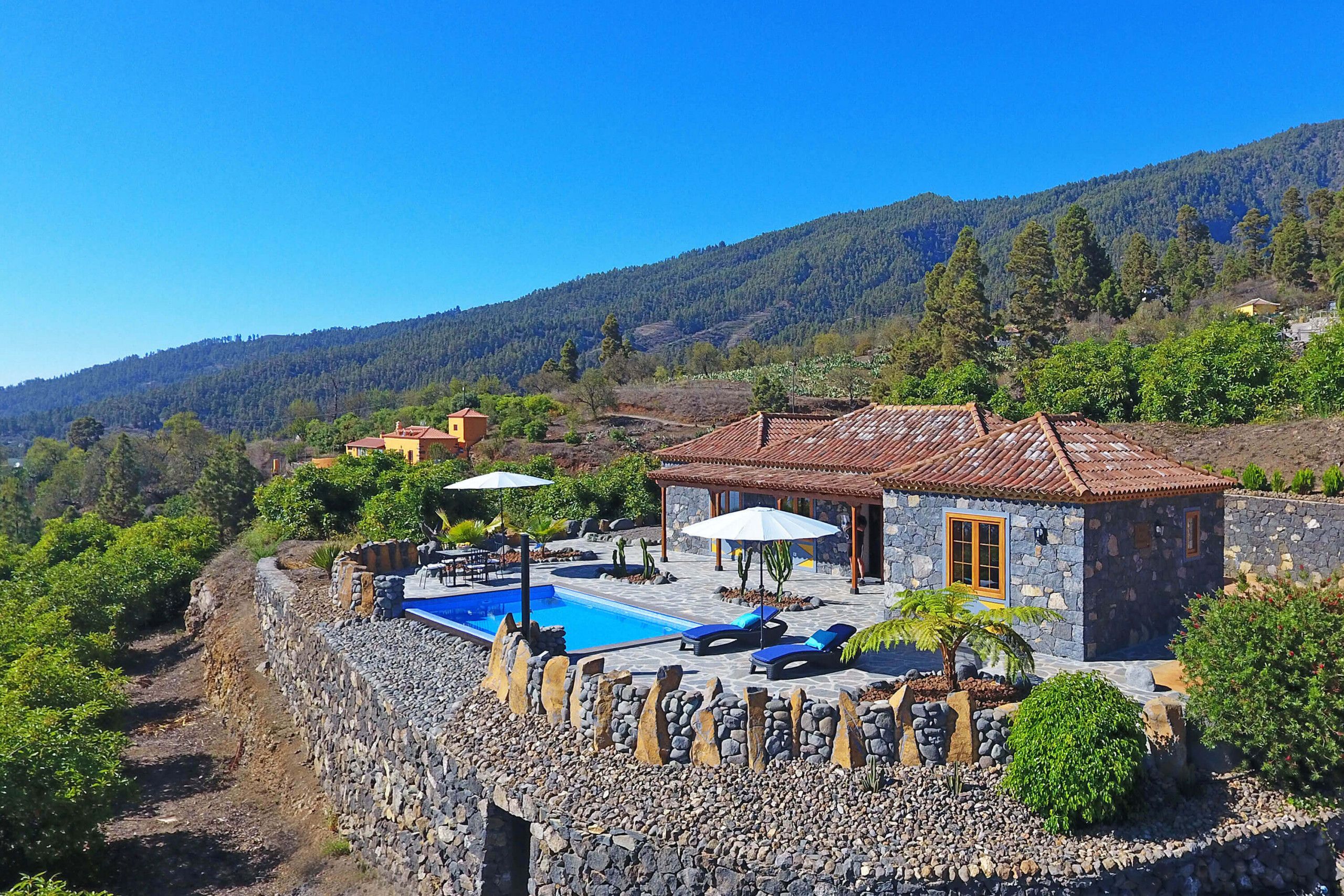 Una casa de piedra con piscina, mobiliario exterior y vistas a un paisaje montañoso.