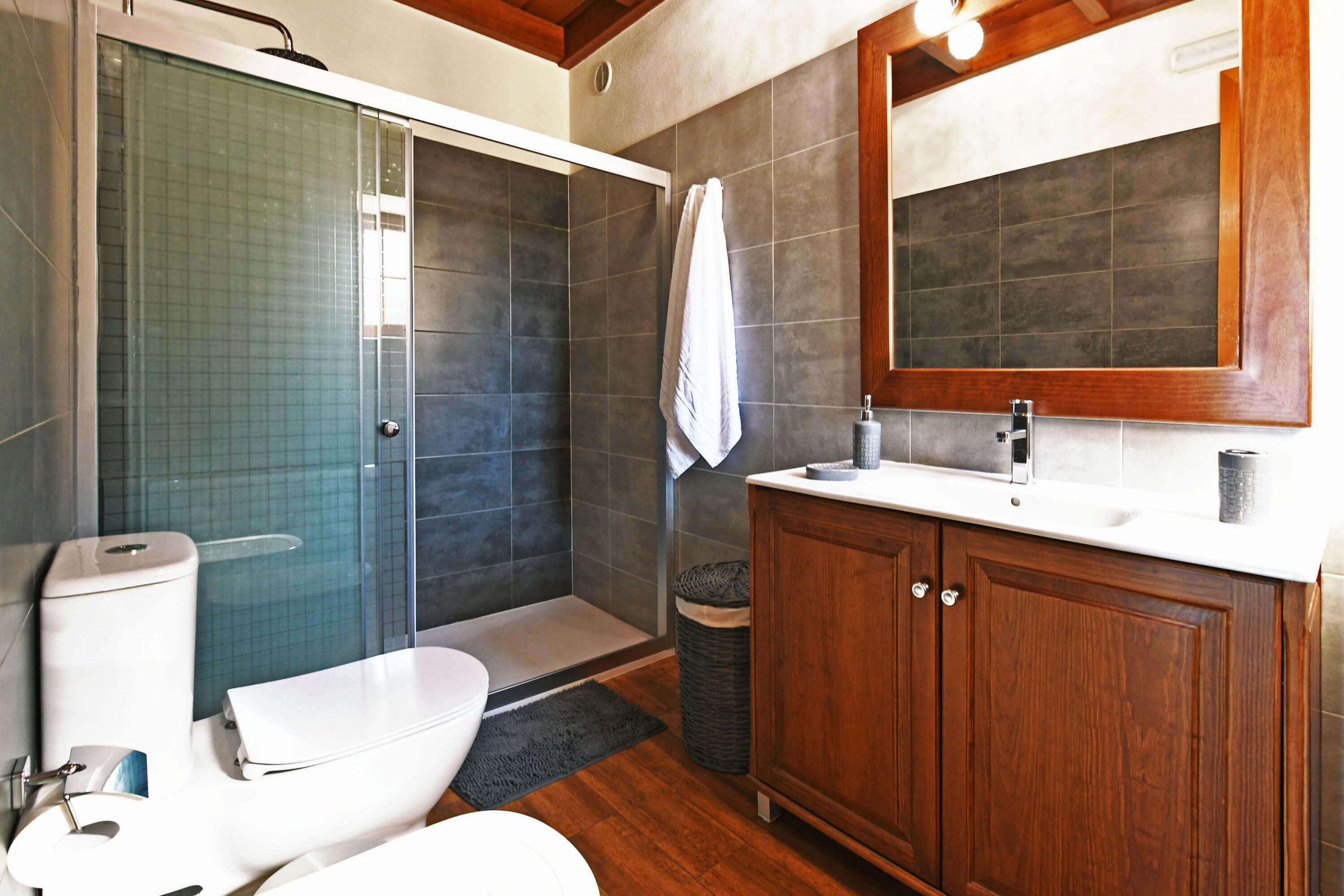 Ein Badezimmer mit Duschkabine aus Glas, Toilette, Waschbecken mit Spiegel und Holzschränken.