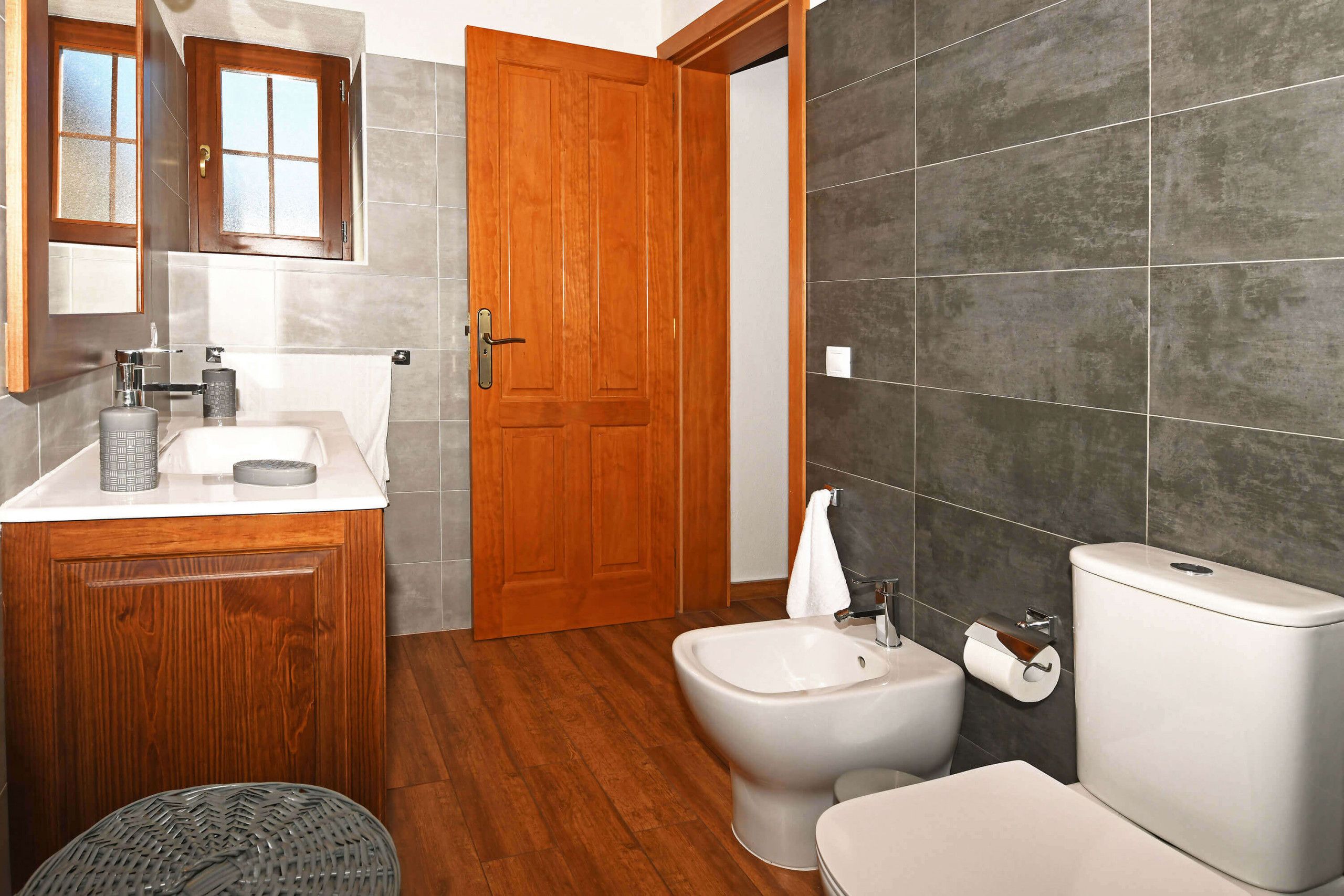 Une salle de bain avec un meuble-lavabo en bois, un bidet, des toilettes et un grand miroir au-dessus du meuble-lavabo.