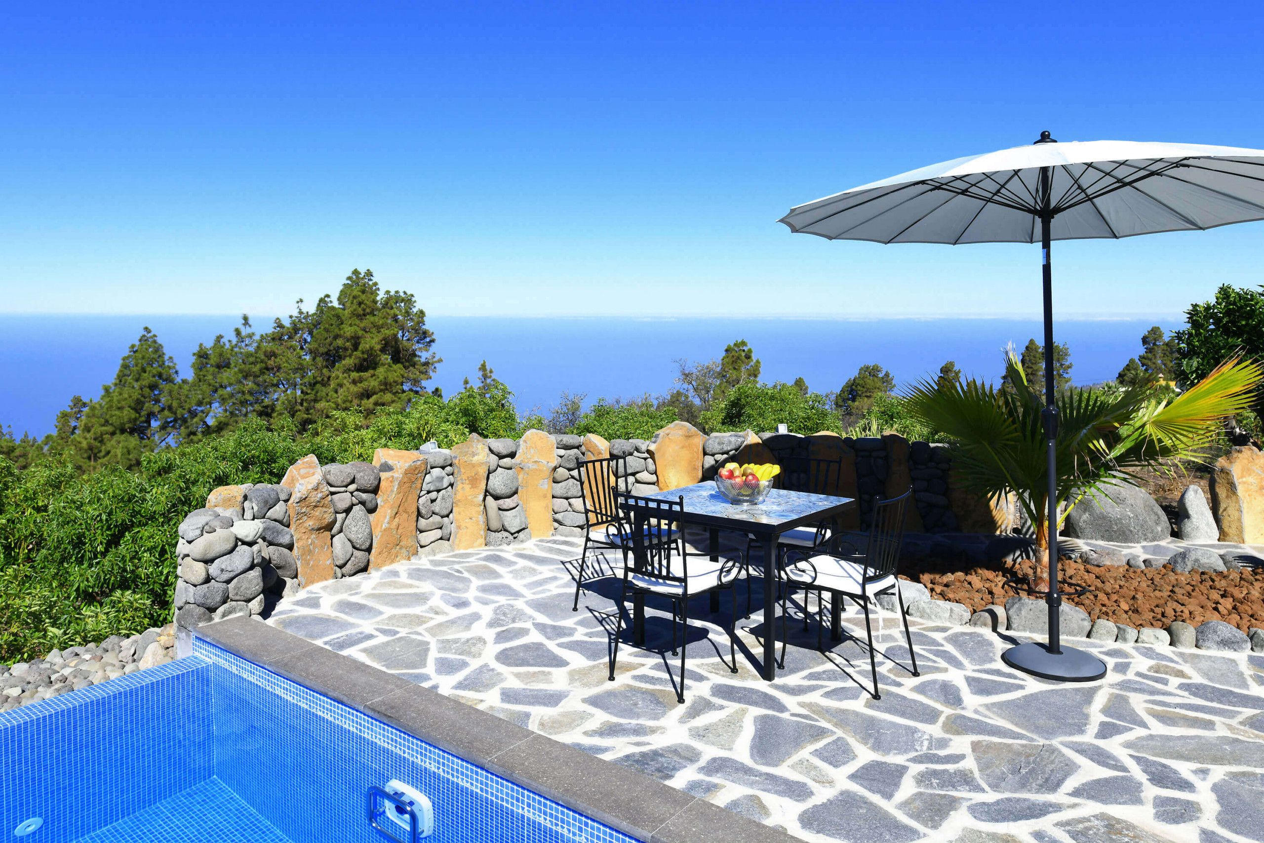 A stone patio with a pool, outdoor seating, and a view of the ocean.