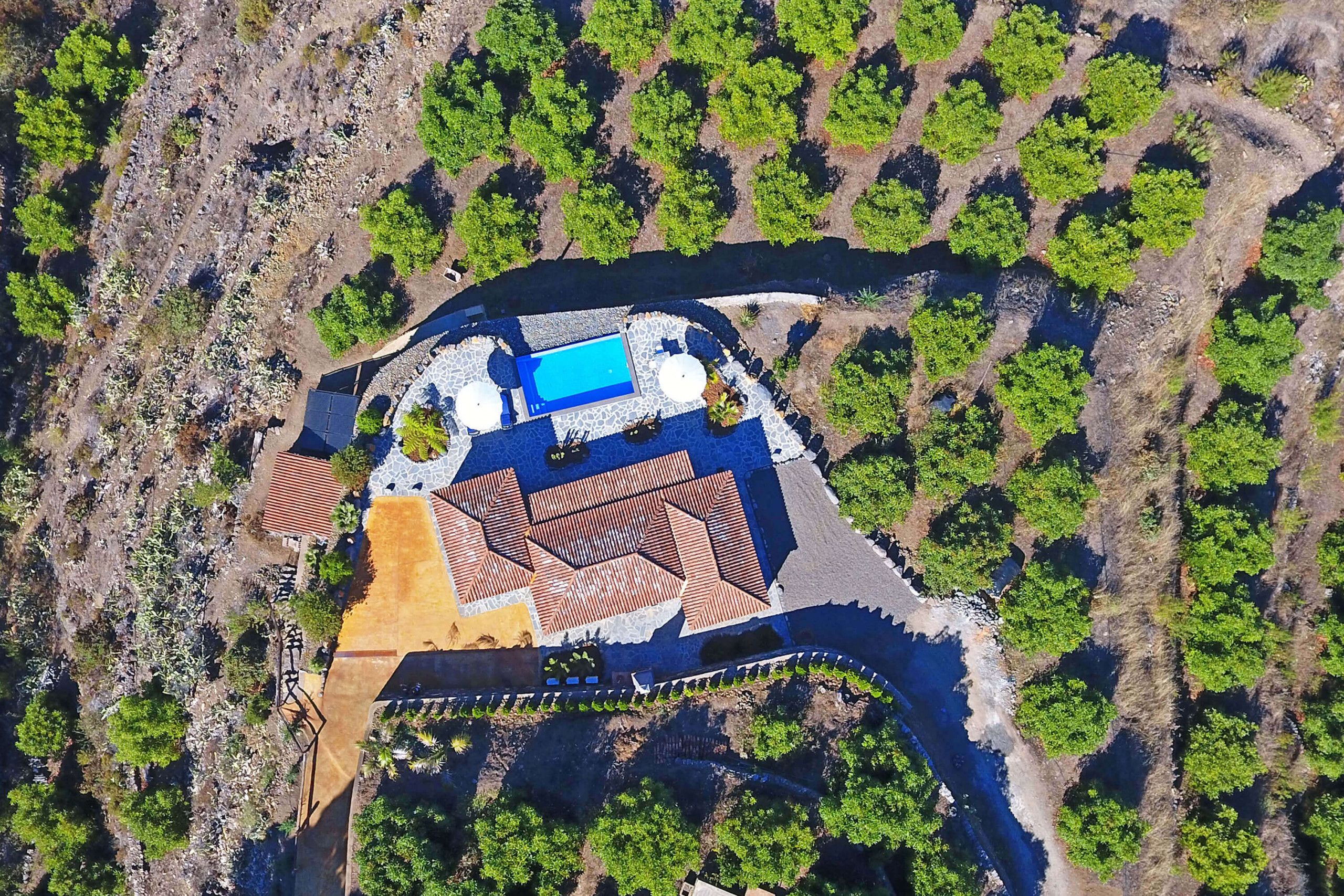 An aerial view of a resort with a swimming pool, multiple buildings, and surrounding greenery.