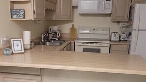 A kitchen with a central island, white cabinets, a microwave, a toaster, and a blender. There are three stools with a light blue design. - Cozy beach townhouse within walking distance to the beach. (Miramar Beach)
