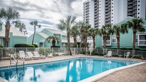 A swimming pool with lounge chairs and palm trees, surrounded by buildings with balconies. - Cozy beach townhouse within walking distance to the beach. (Miramar Beach)