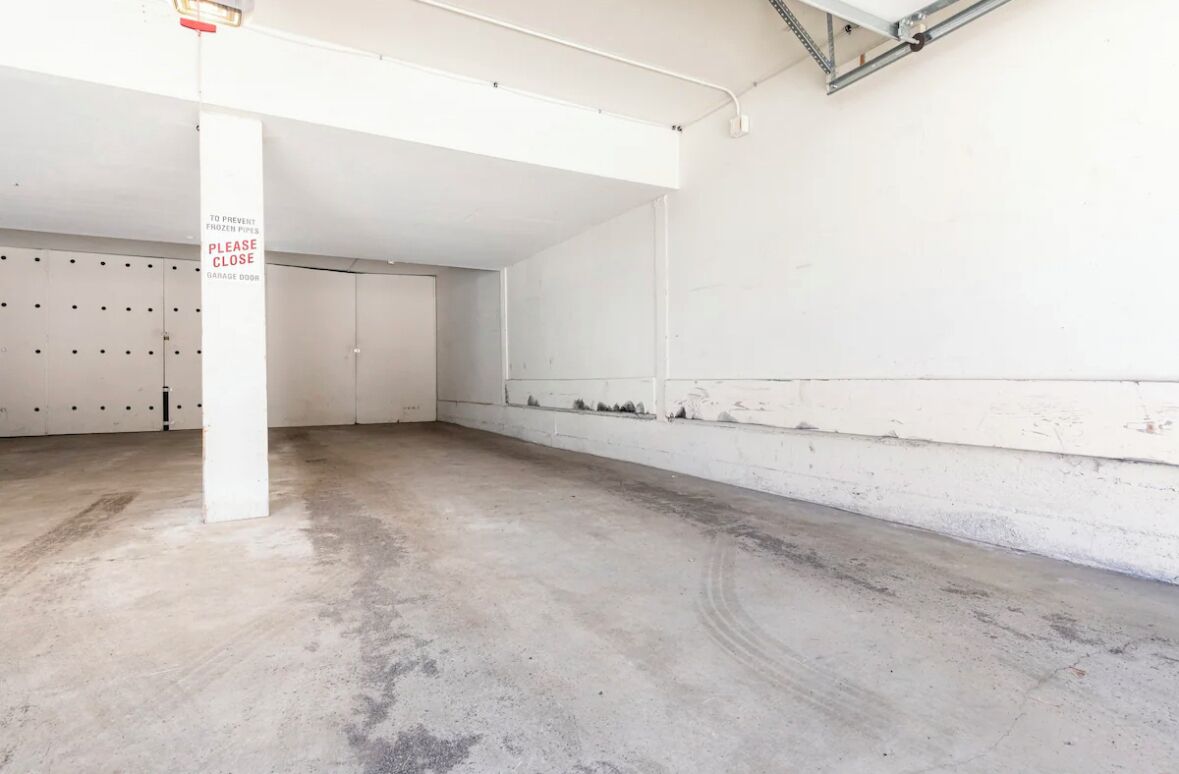 Un garage vide, sur lequel est affiché un panneau indiquant qu’il faut empêcher le gel des tuyaux en gardant la porte du garage fermée.