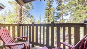 Una terraza de madera con dos sillas Adirondack, rodeada de árboles altos.
