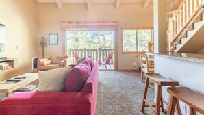 Una sala de estar acogedora con un sofá rojo, una escalera de madera y un amplio ventanal con vistas al exterior.