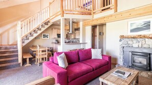 Una sala de estar acogedora con una escalera de madera, un sofá rosa, una chimenea y un comedor.