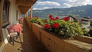 A wooden balcony with checkered tablecloths and chairs, wooden railings, and red flowers. - Sportpension Christina (Fuegen)