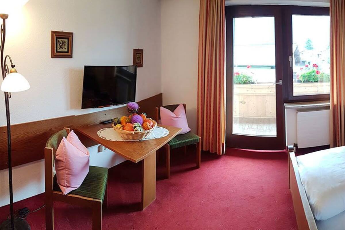 A hotel room with a bed, a desk with a chair, a TV, and a window with curtains.