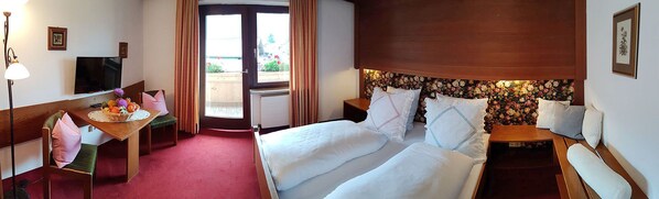 Habitación de hotel con cama, escritorio, silla, televisor y ventana con cortinas.