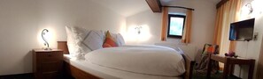 Un dormitorio con cama, mesita de noche, lámpara, ventana y televisor en la pared.