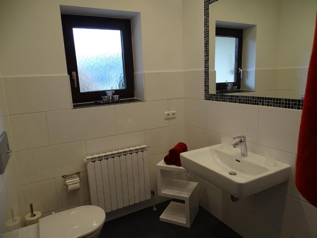 Ein Badezimmer mit Toilette, Waschbecken, Spiegel, Fenster und Heizkörper.