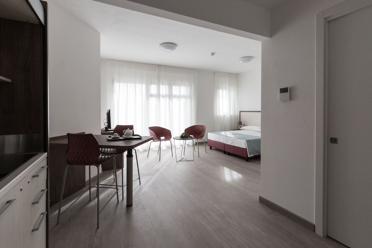 Una stanza moderna e luminosa con angolo ristoro, un letto e angolo cottura.