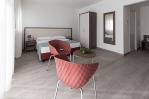 A modern hotel room with a bed, a red chair, a small table with a fruit bowl, and a wardrobe.