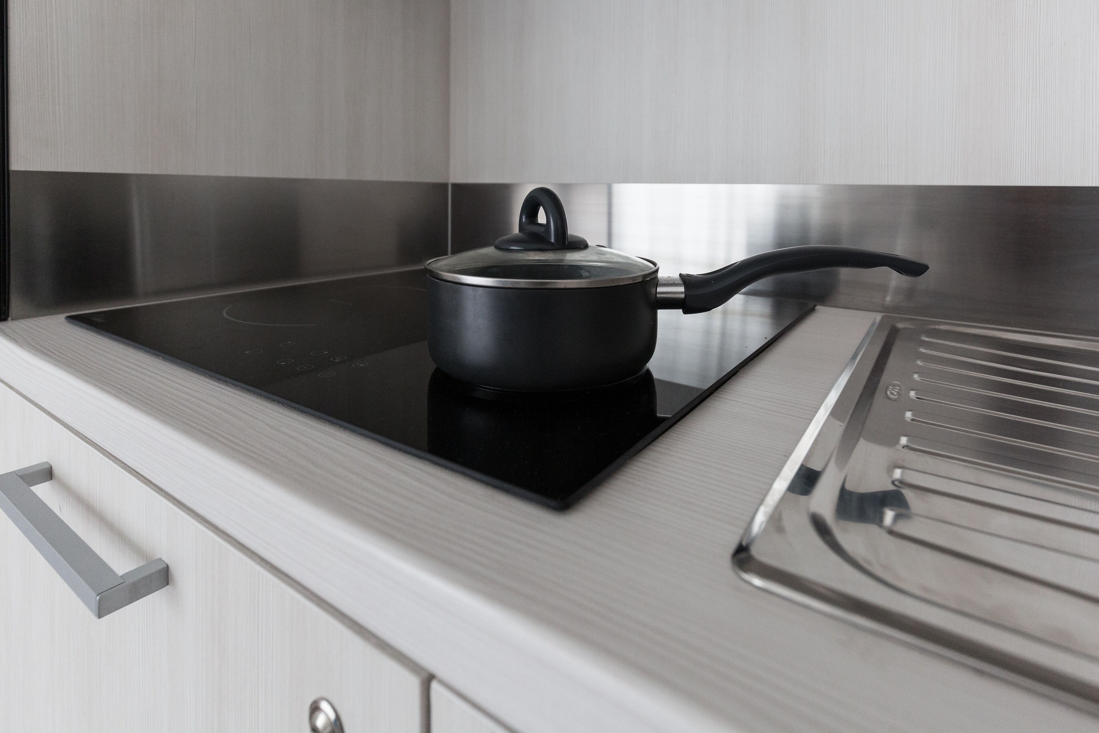 A kitchen with a stovetop, a pot, and a modern stainless steel cabinet.