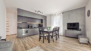 Une cuisine moderne dotée d’appareils électroménagers intégrés, un coin repas avec une table dressée pour quatre personnes, et un téléviseur à écran plat fixé à un meuble.