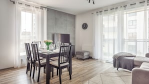 Un espace repas moderne avec une table ronde dressée pour quatre personnes, entourée de chaises en bois foncé. Un vase contenant des fleurs blanches est posé sur la table.