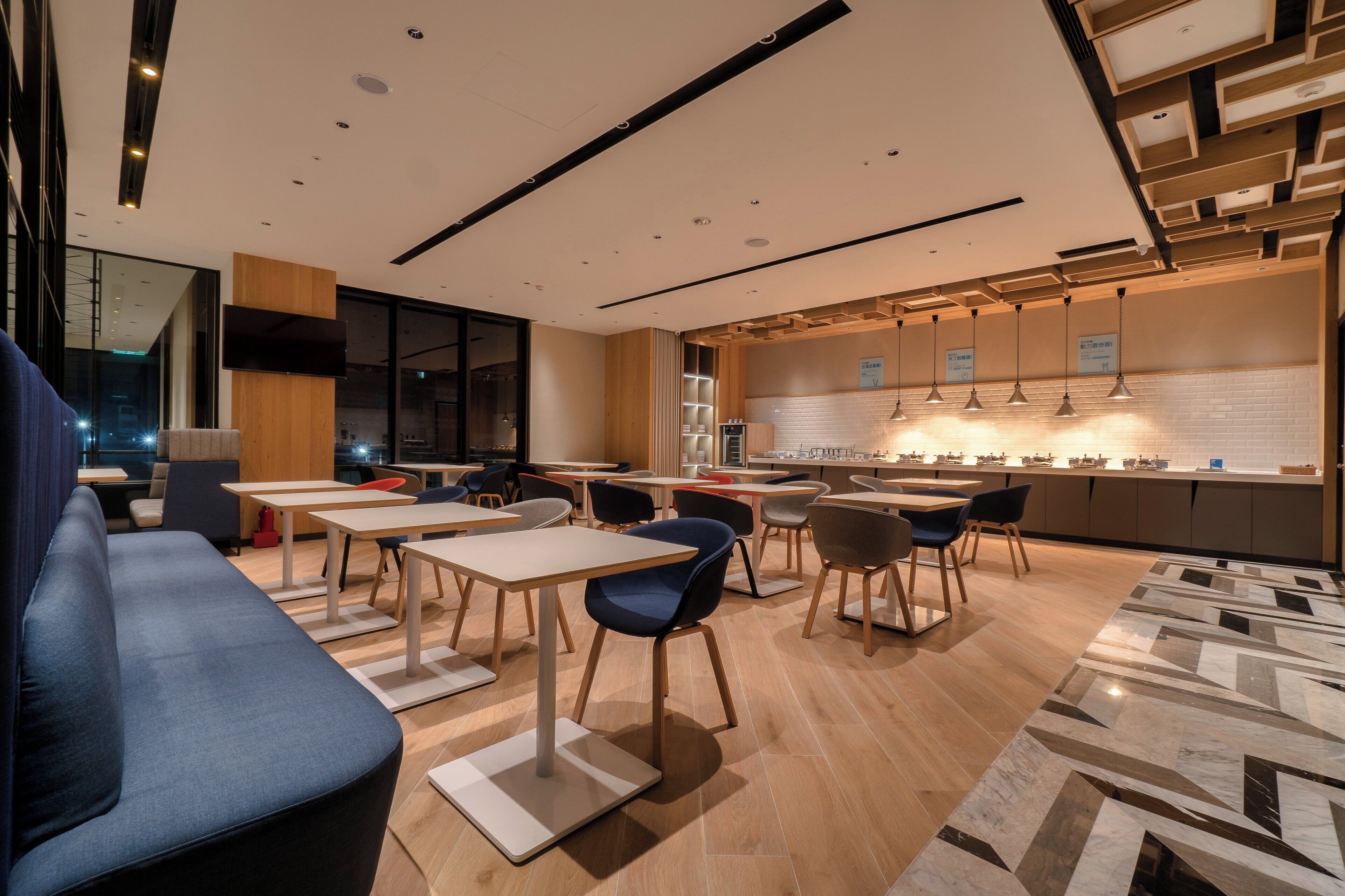A modern dining area with tables and chairs, a kitchen counter, and a seating area with a sofa.