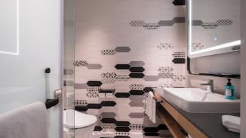 A modern bathroom with a geometric tile backsplash, a glass shower enclosure, and a vanity with a mirror.