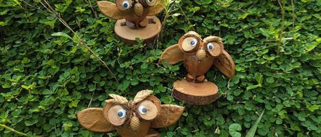 Three wooden owl sculptures on tree stumps surrounded by green foliage.