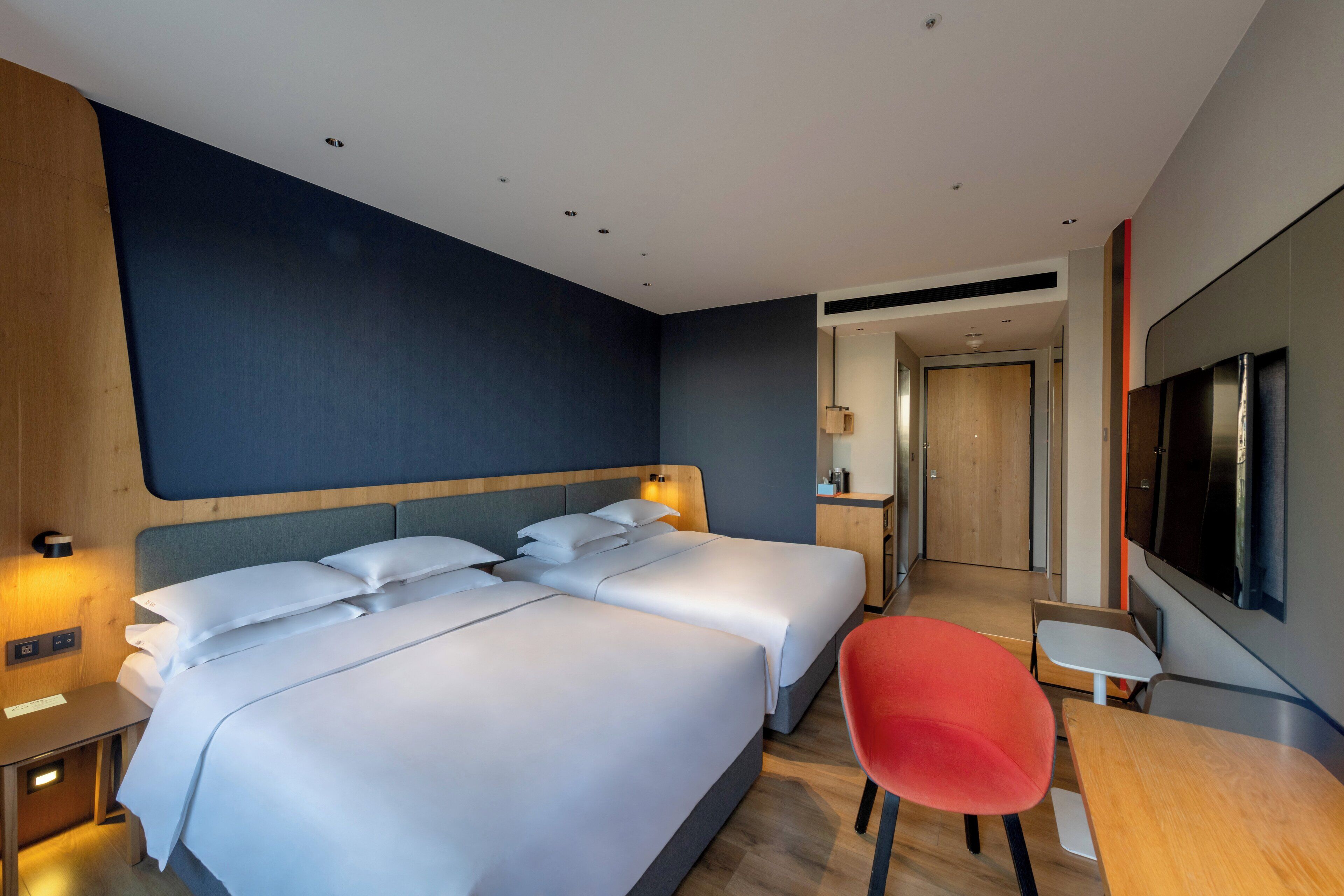 Habitación de hotel con dos camas, un escritorio, una silla, un televisor y piso de madera.