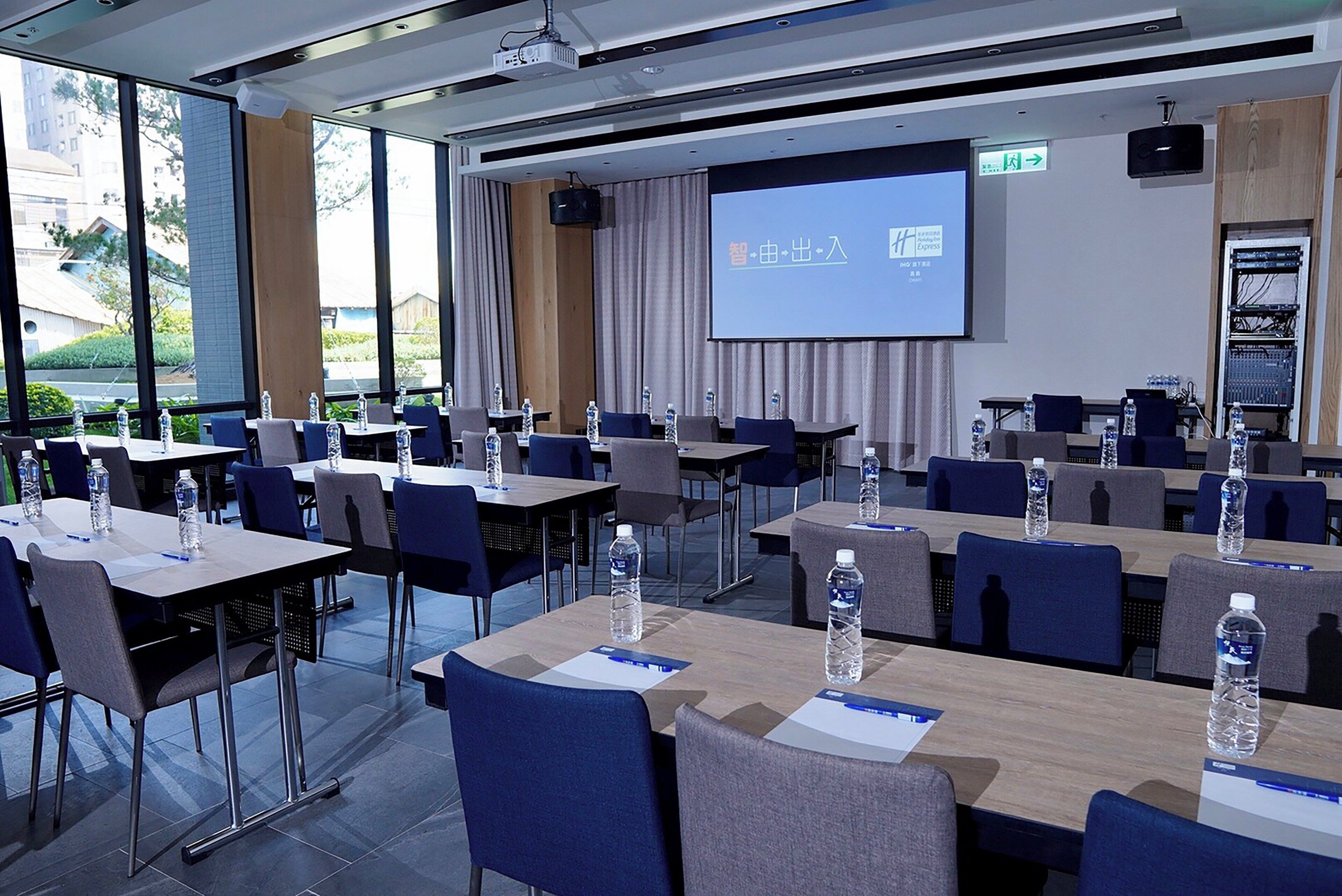 A conference room with tables and chairs, a projector screen, and a large window.