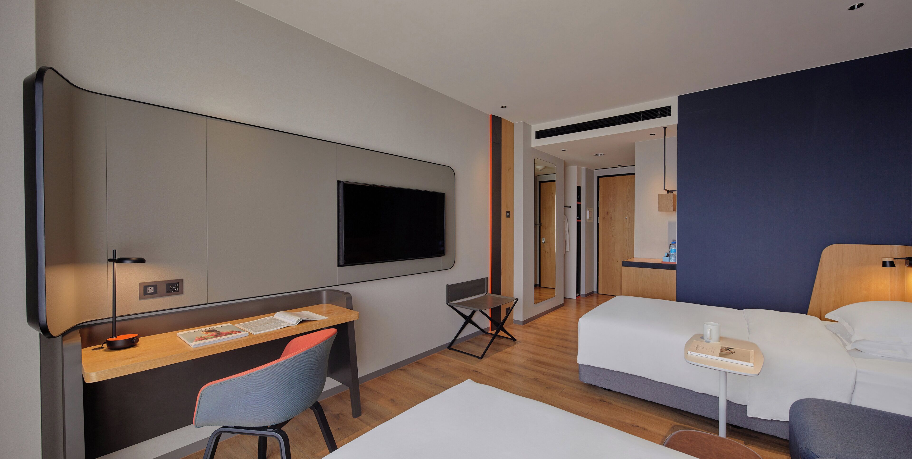 Quarto de hotel com escrivaninha, cadeira, cama e televisão.