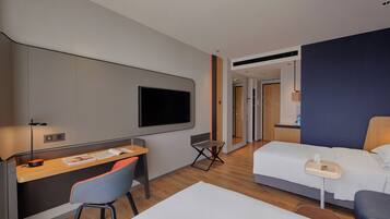 Quarto de hotel com escrivaninha, cadeira, cama e televisão.