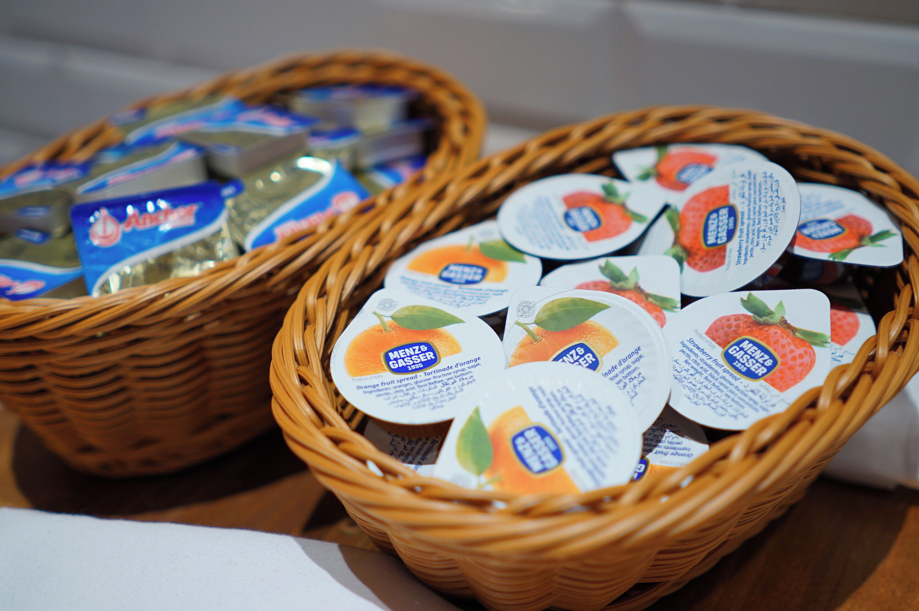 Two wicker baskets filled with packaged food items, one with orange spread and the other with strawberry spread.