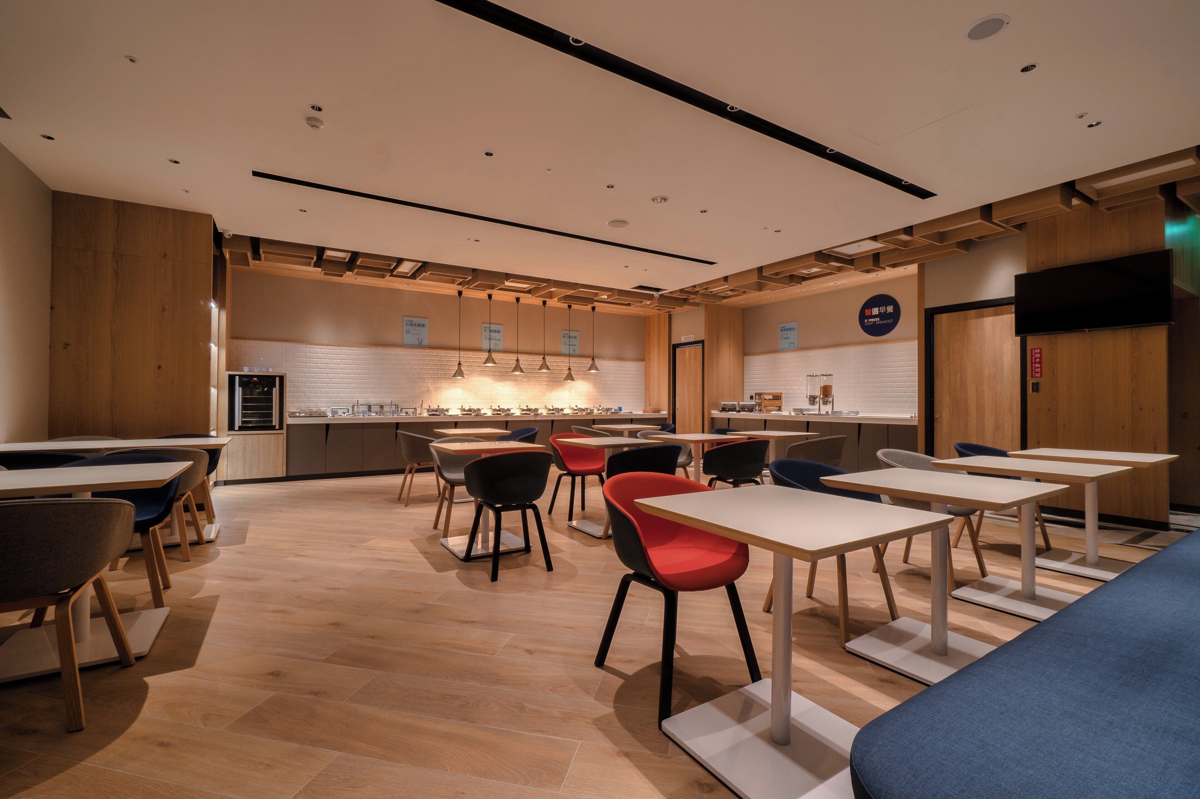 Un espace de restauration moderne avec un plancher en bois, plusieurs tables et chaises, et une cuisine en arrière-plan.